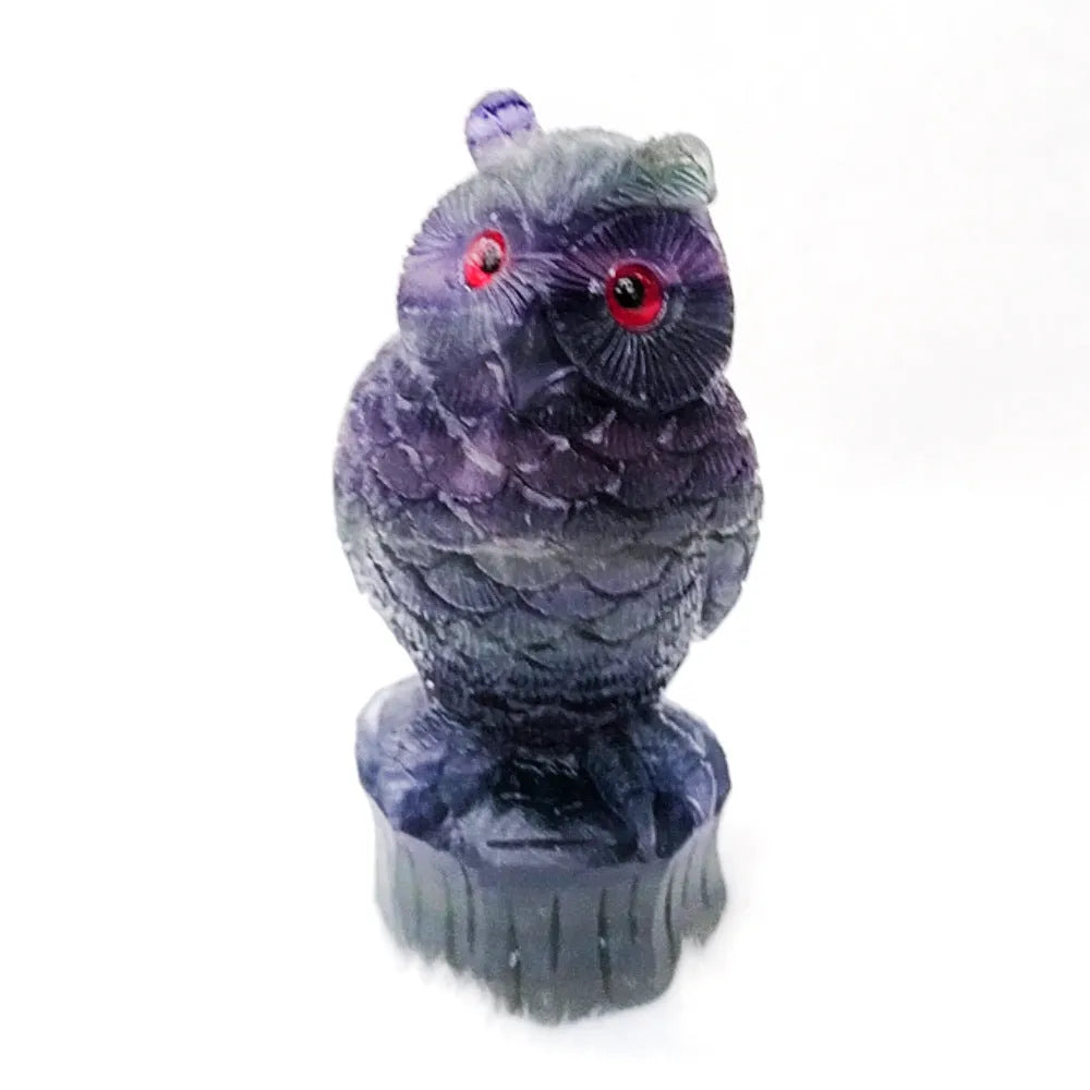 Hand-carved purple fluorite owl ornament on display surface showing natural colour variations