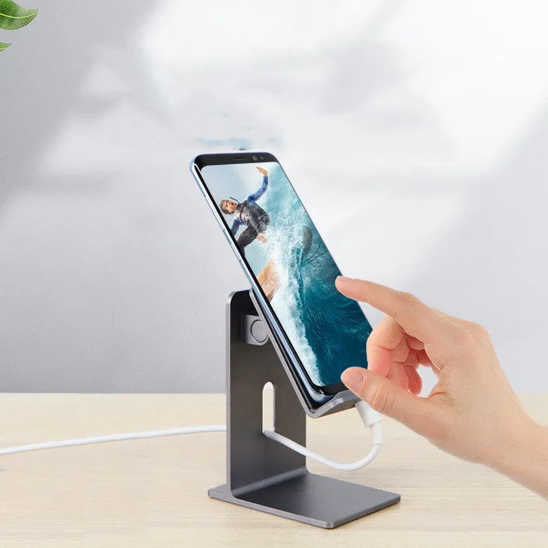 Dark space grey aluminium mobile phone holder with adjustable clamp and 360-degree ball joint on a wooden desk.