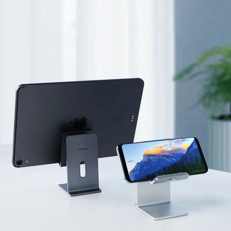 Dark space grey aluminium mobile phone holder with adjustable clamp and 360-degree ball joint on a wooden desk.
