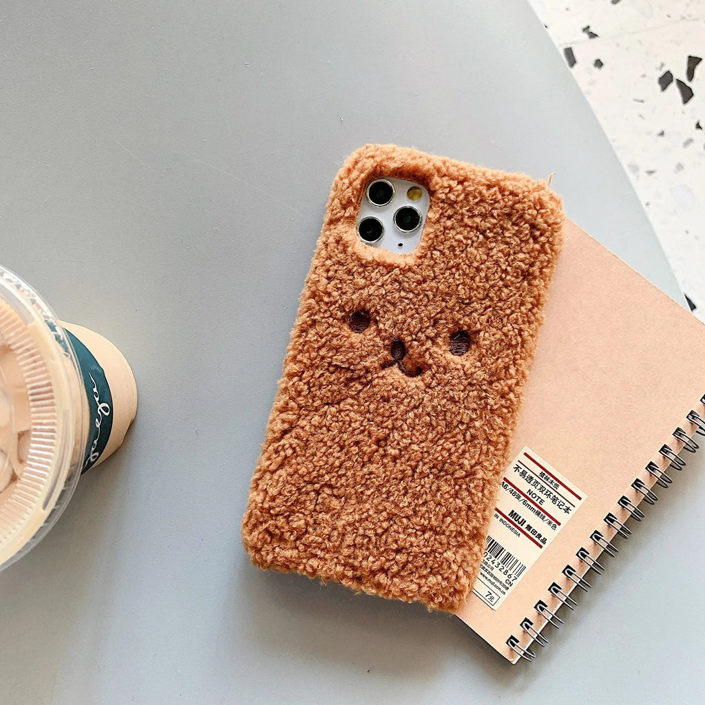 Brown embroidered plush bear face on a soft TPU phone case for iPhone, showing camera cut-out and raised edges.