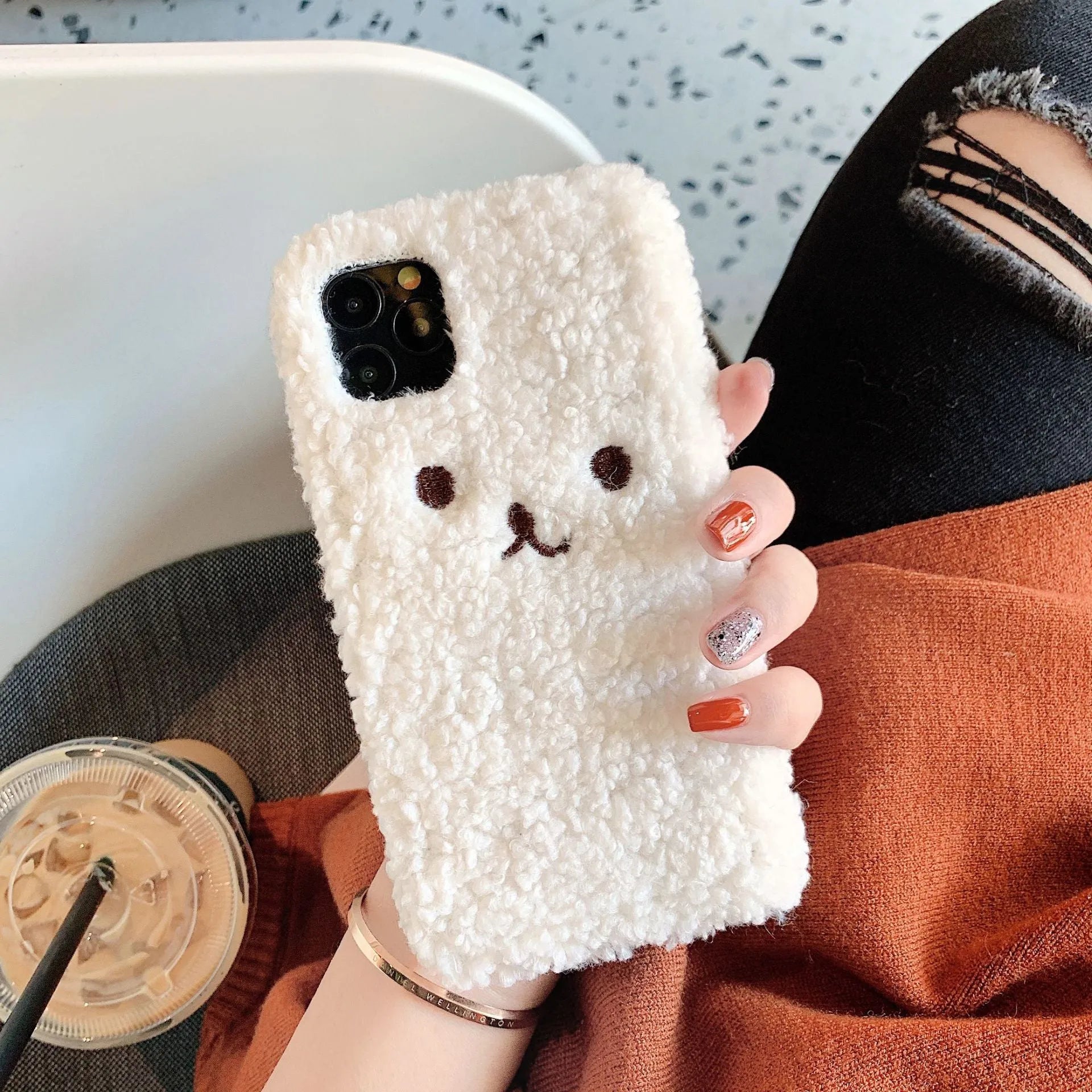 Brown embroidered plush bear face on a soft TPU phone case for iPhone, showing camera cut-out and raised edges.