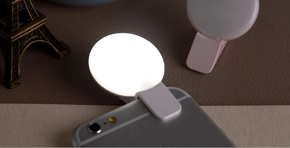 Round white mobile phone fill light clipped onto a smartphone for selfies.