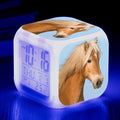 Small square colour changing alarm clock with LED digital display on a desk.