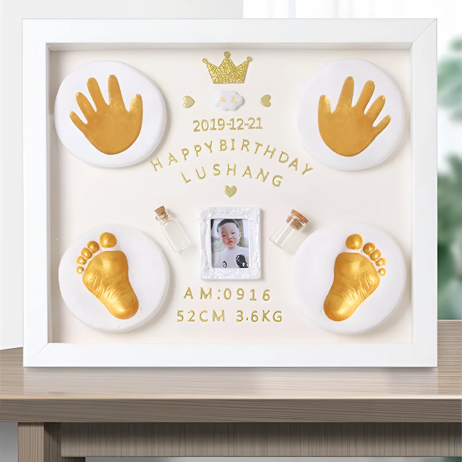 Modern DIY baby hand and foot photo frame in white on a shelf, showing handprint and footprint display area.