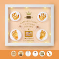 Modern DIY baby hand and foot photo frame in white on a shelf, showing handprint and footprint display area.