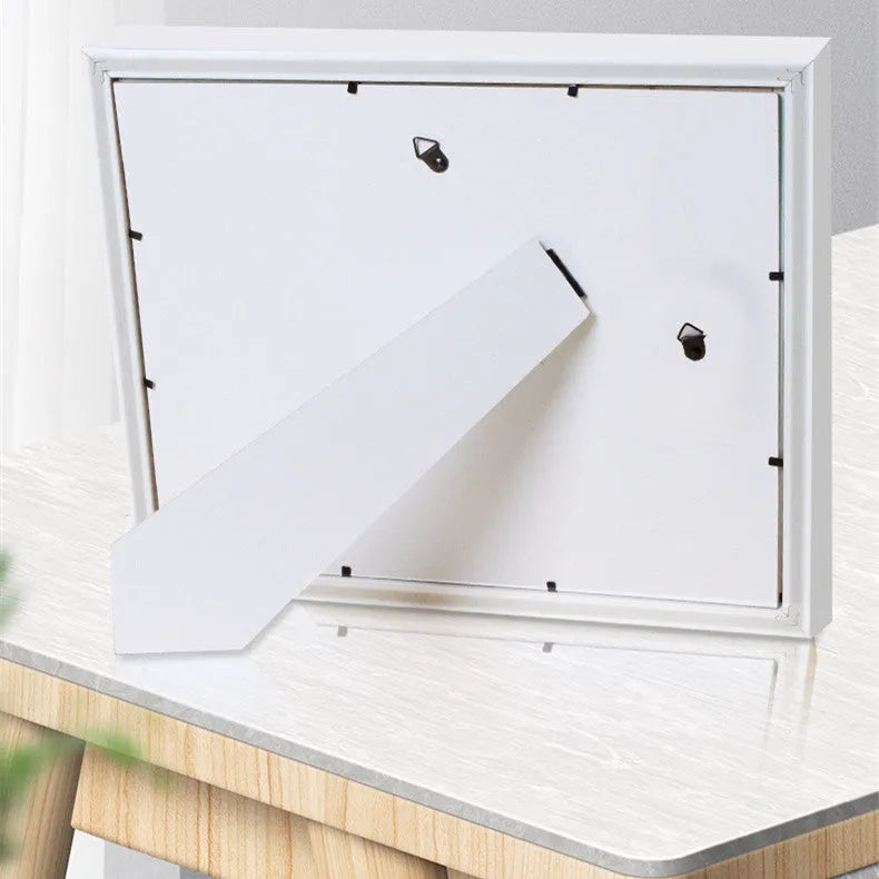 Modern DIY baby hand and foot photo frame in white on a shelf, showing handprint and footprint display area.