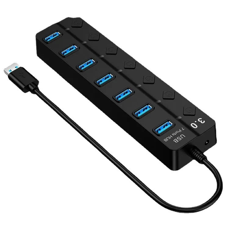 Black 7-port USB 3.0 hub with individual power switches and external power adapter on a wooden desk.