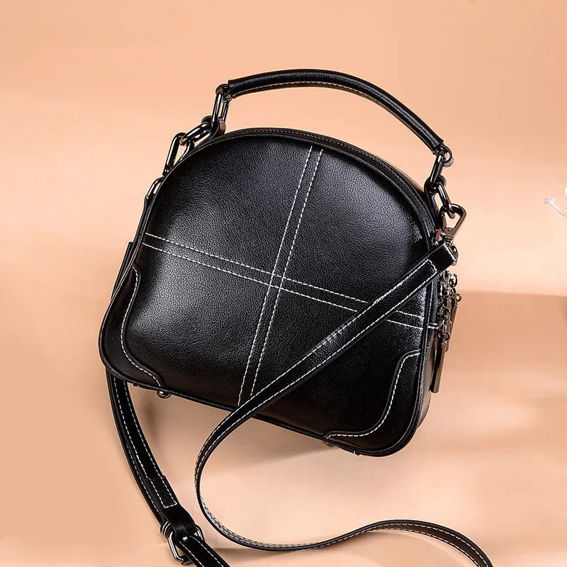 Round leather shoulder bag in wine red with soft handles and a zipper closure.