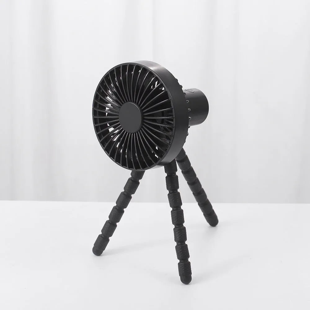 A small black adjustable desktop fan with flexible octopus tripod legs and a bending head on a wooden desk.