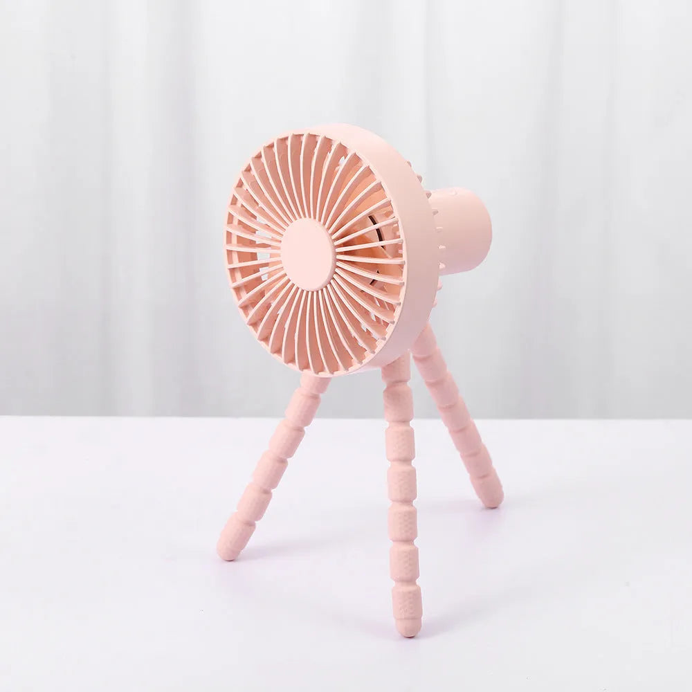A small black adjustable desktop fan with flexible octopus tripod legs and a bending head on a wooden desk.