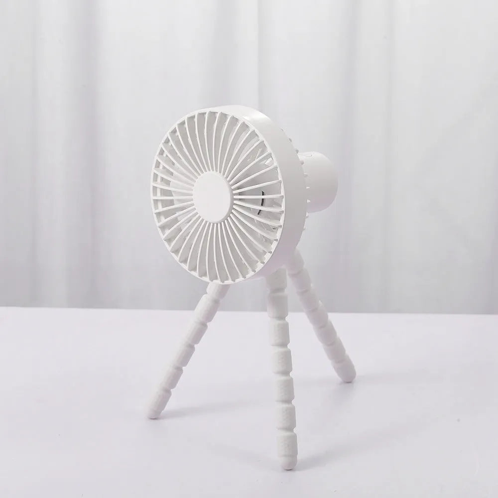A small black adjustable desktop fan with flexible octopus tripod legs and a bending head on a wooden desk.
