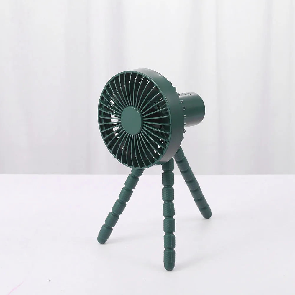 A small black adjustable desktop fan with flexible octopus tripod legs and a bending head on a wooden desk.