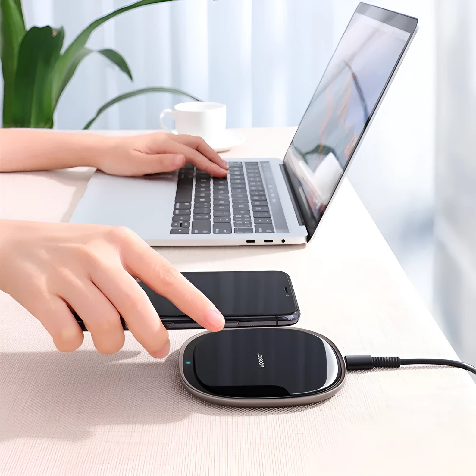 Black 15W wireless charging pad with glass top on a wooden desk next to a mobile phone.