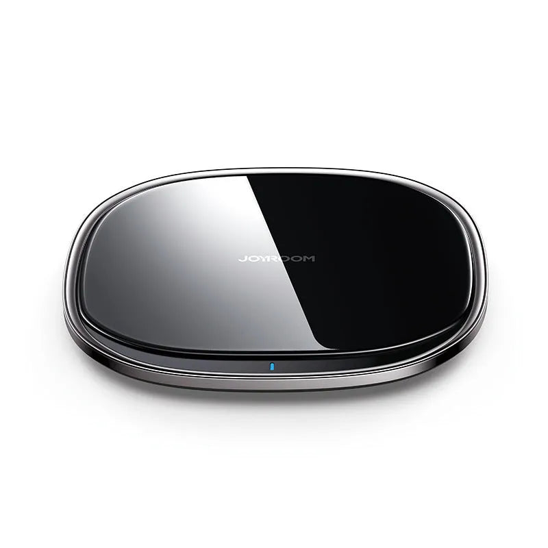 Black 15W wireless charging pad with glass top on a wooden desk next to a mobile phone.