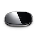 Black 15W wireless charging pad with glass top on a wooden desk next to a mobile phone.