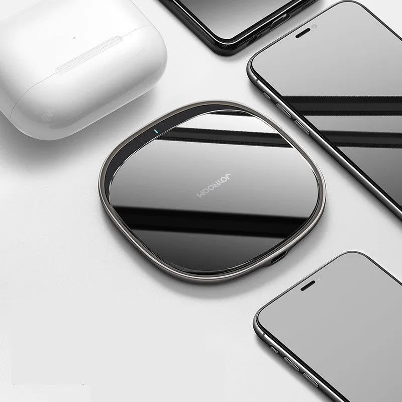 Black 15W wireless charging pad with glass top on a wooden desk next to a mobile phone.