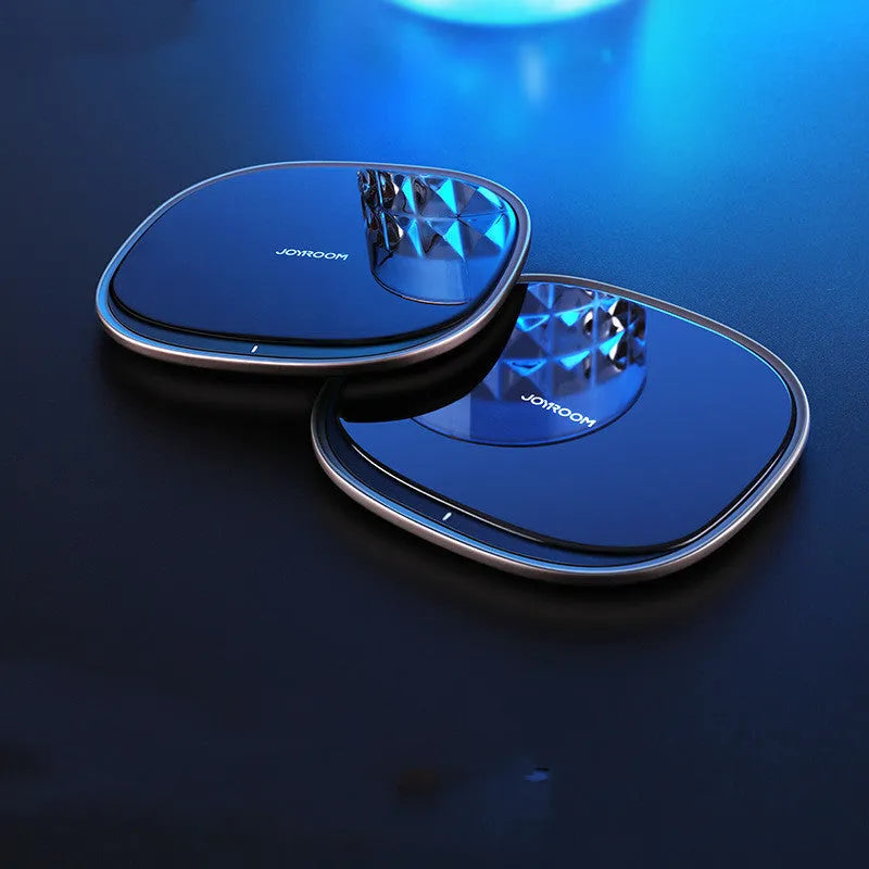 Black 15W wireless charging pad with glass top on a wooden desk next to a mobile phone.