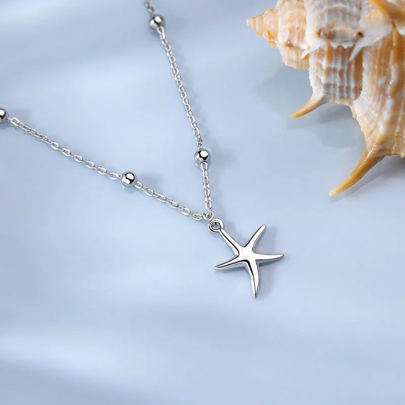 Close-up of a sterling silver anklet with a small starfish charm on a chain of tiny round beads.