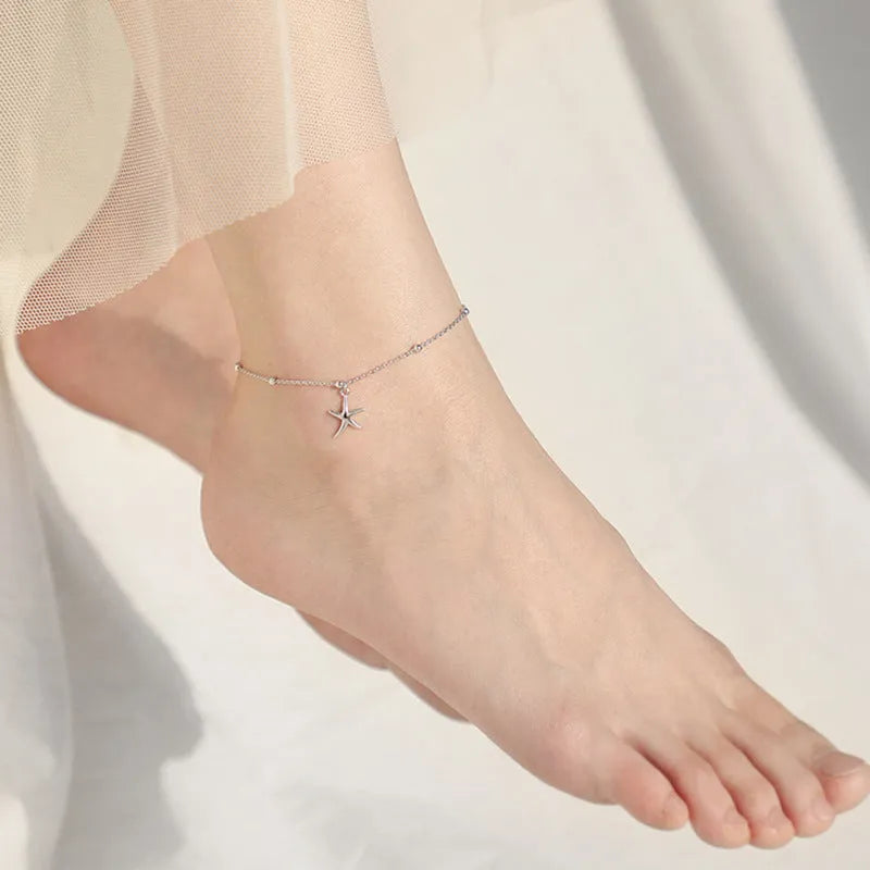Close-up of a sterling silver anklet with a small starfish charm on a chain of tiny round beads.