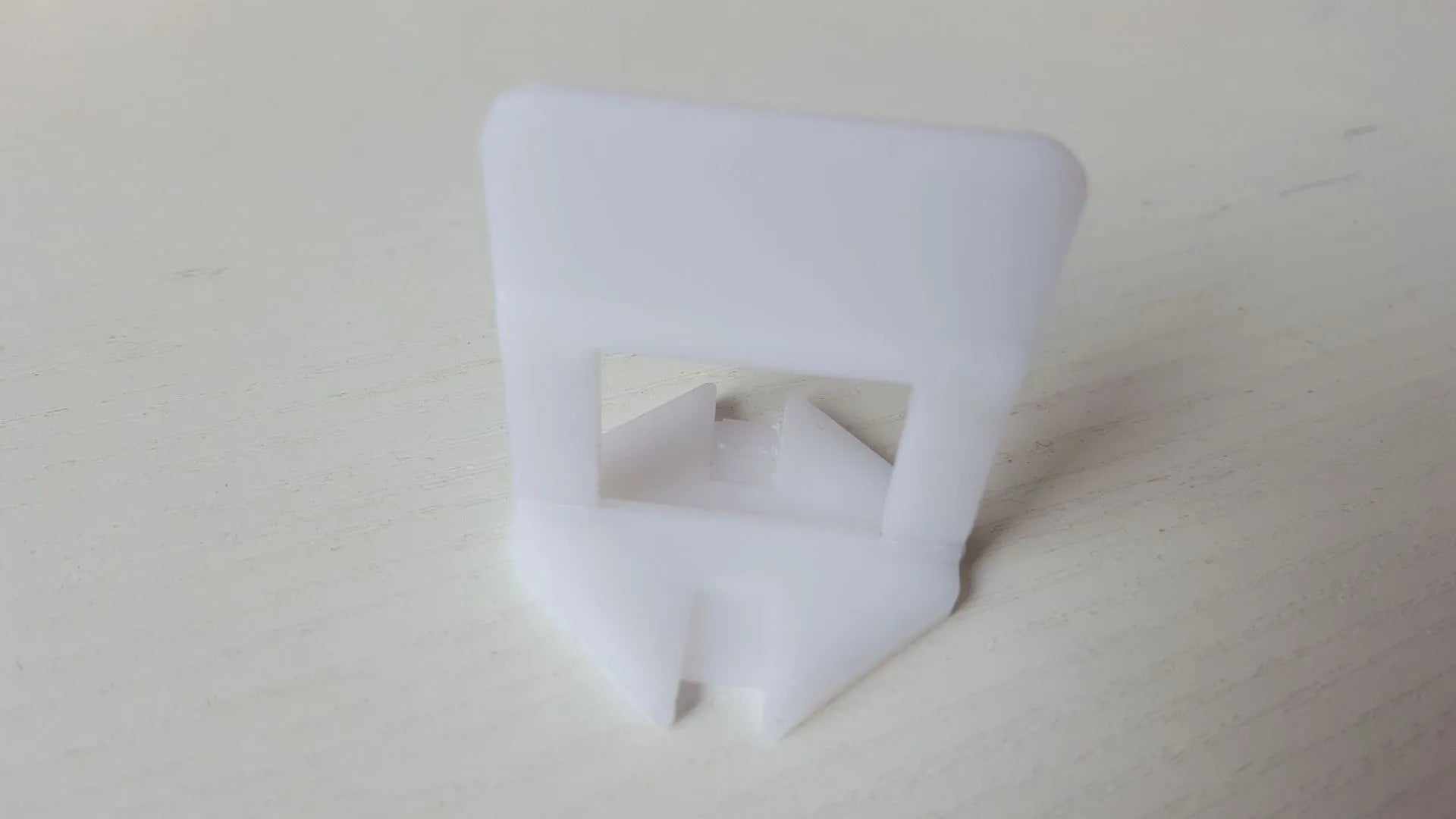 Orange plastic tile leveling wedges and white base clips on a tiled floor, with a rubber hammer nearby