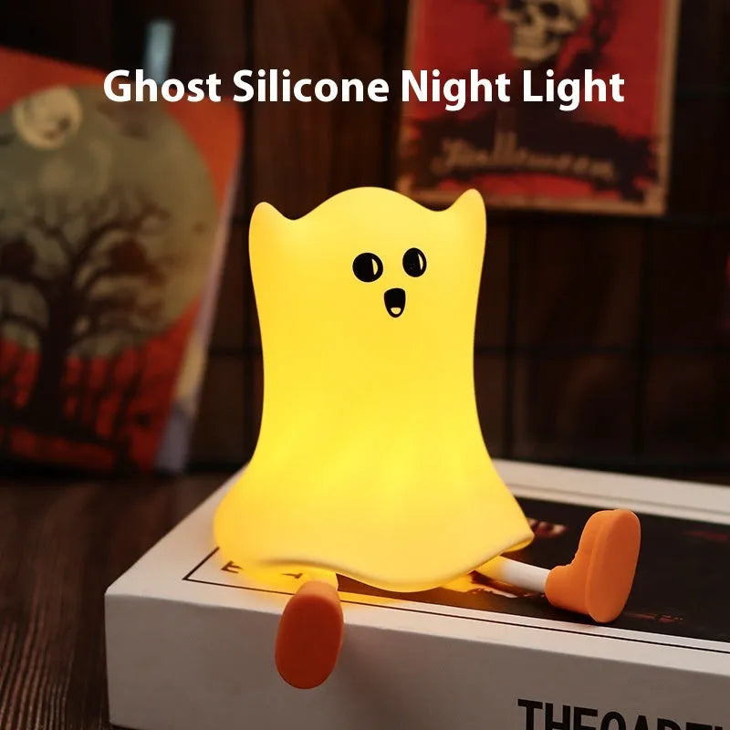 Ghost shaped silicone bedside lamp with touch control emitting soft yellow glow on a bedside table