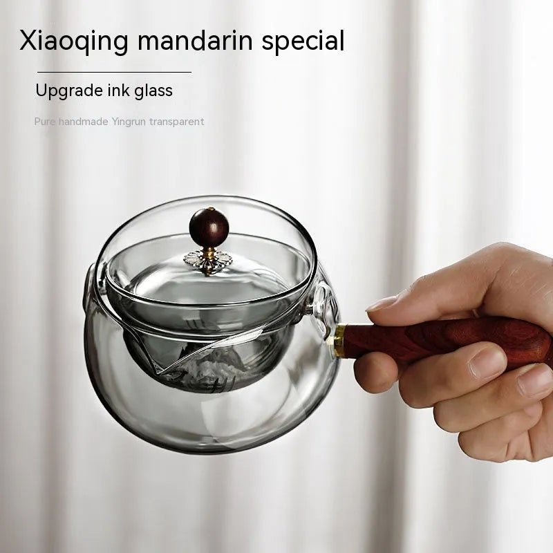 Grey and transparent rotary glass teapot with wooden handle and infuser on a kitchen counter