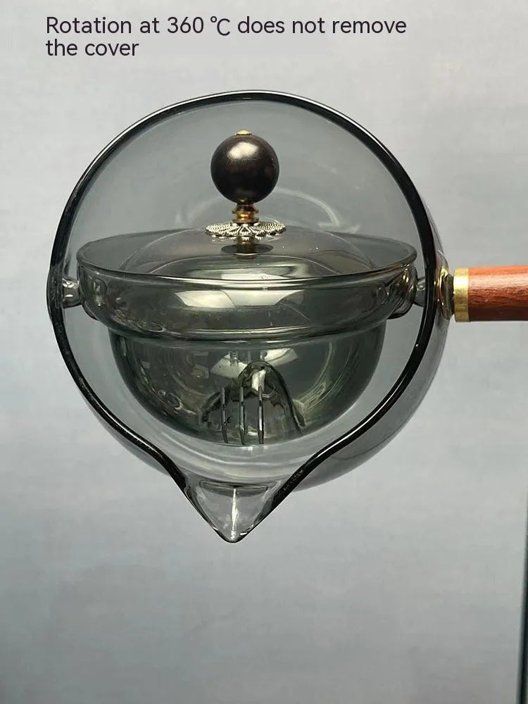 Grey and transparent rotary glass teapot with wooden handle and infuser on a kitchen counter