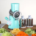 Blue green mandoline vegetable cutter with three stainless steel blades and rubber sucker base on kitchen counter