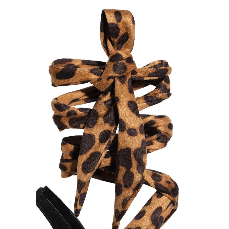 Light brown leopard print women's Roman sandals with cross-straps and a tall stiletto heel on a neutral background.