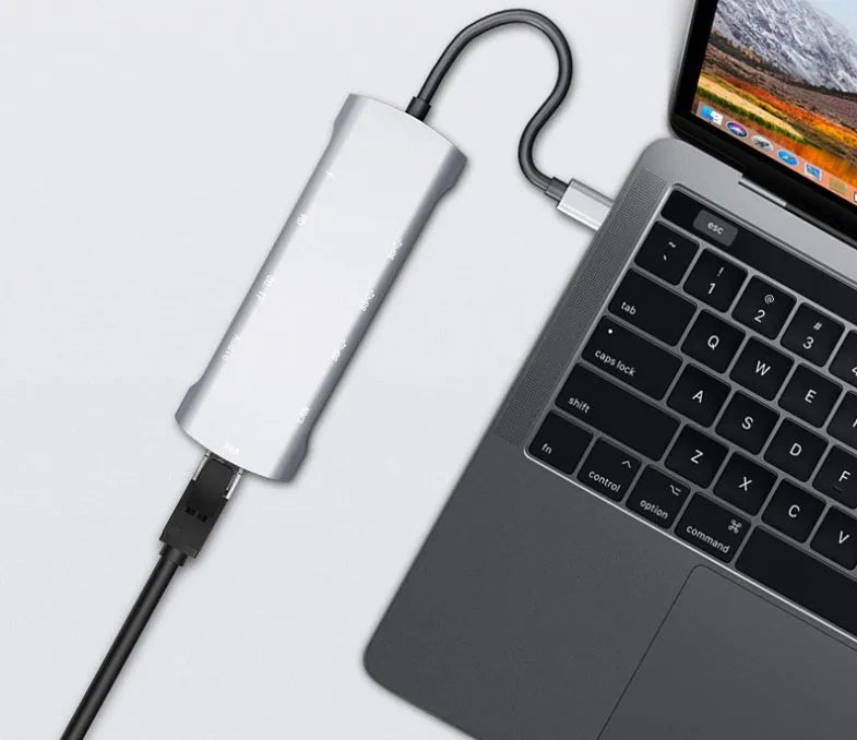 Grey aluminium USB-C docking station with HDMI, VGA, USB 3.0, and PD charging ports on a desk.