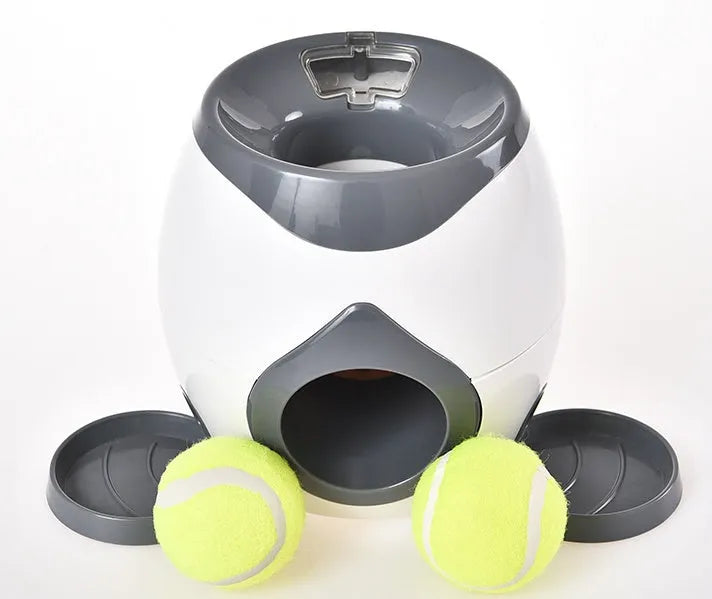 Smart pet feeder reward machine with two tennis balls and treat dispenser in green and white colour, shown on a wooden floor