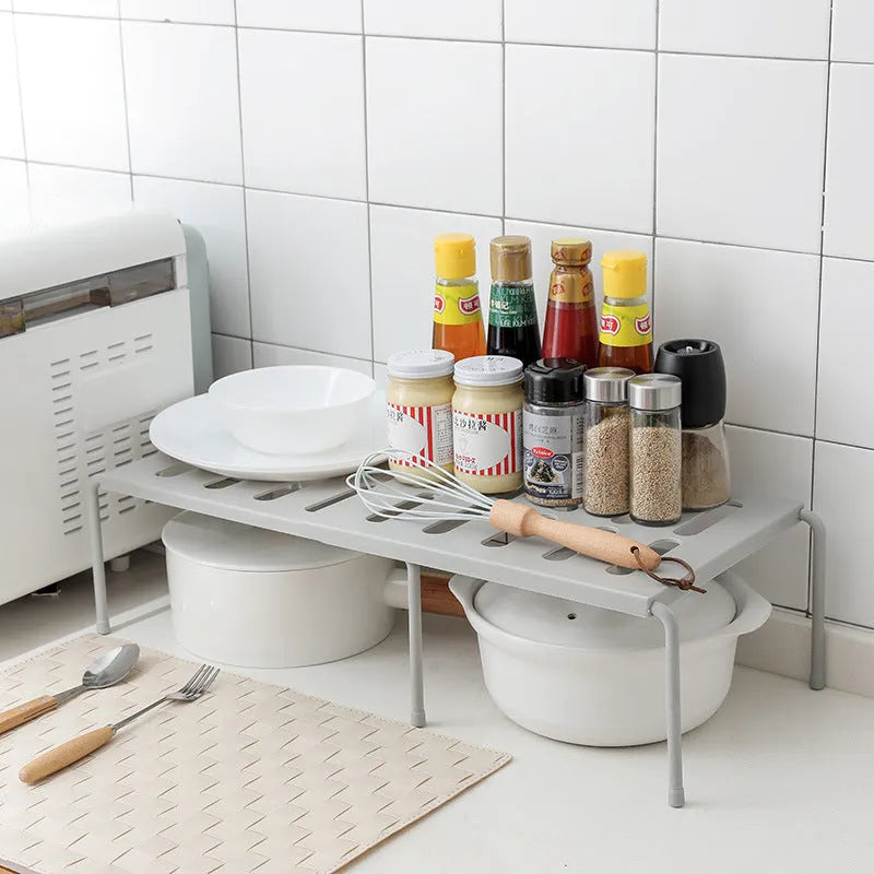 White telescopic plastic storage rack extended to full height with kitchen utensils organised on shelf