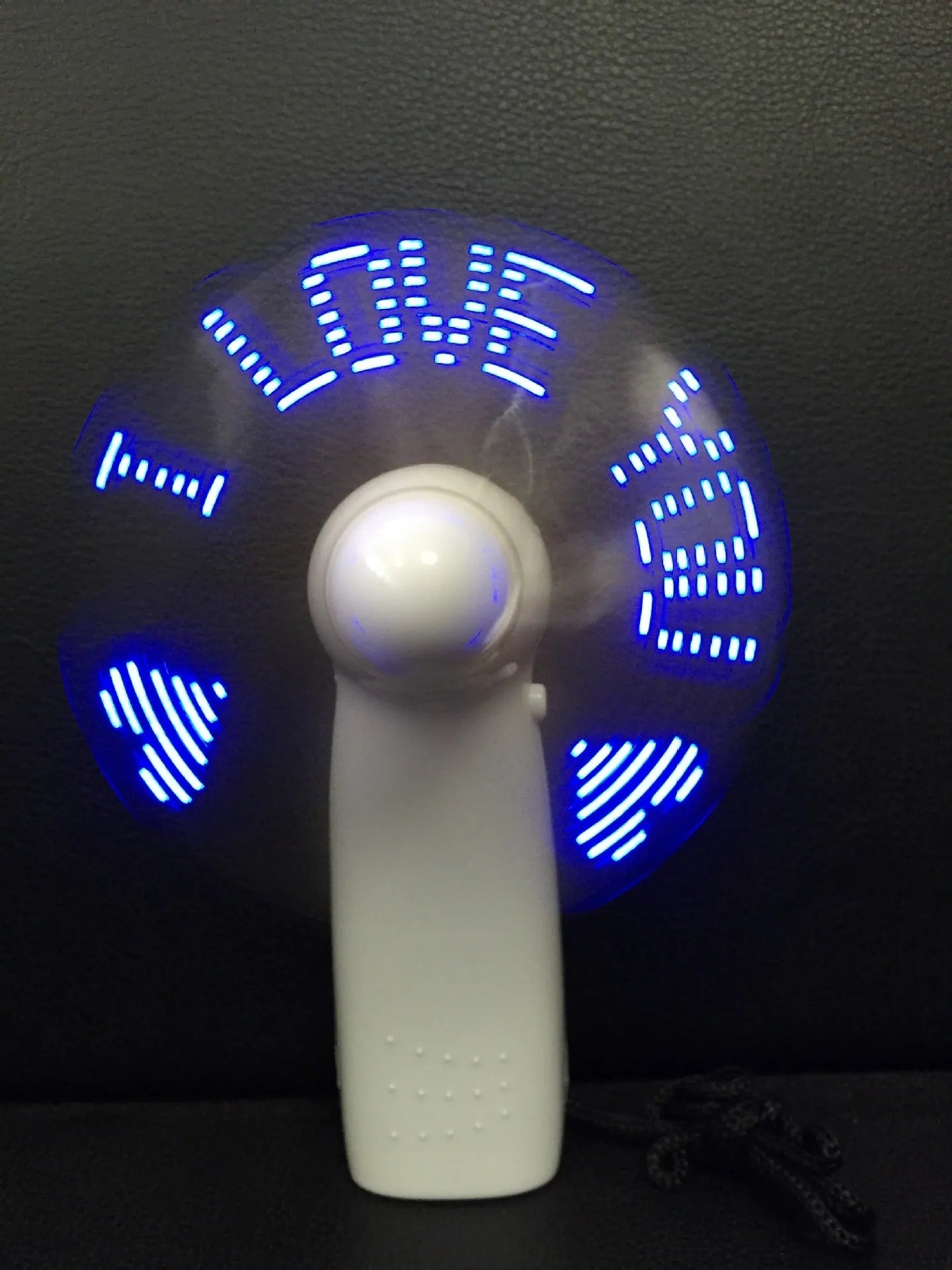 White handheld mini fan with flashing blue and red LED 'I Love You' pattern on a dark background.