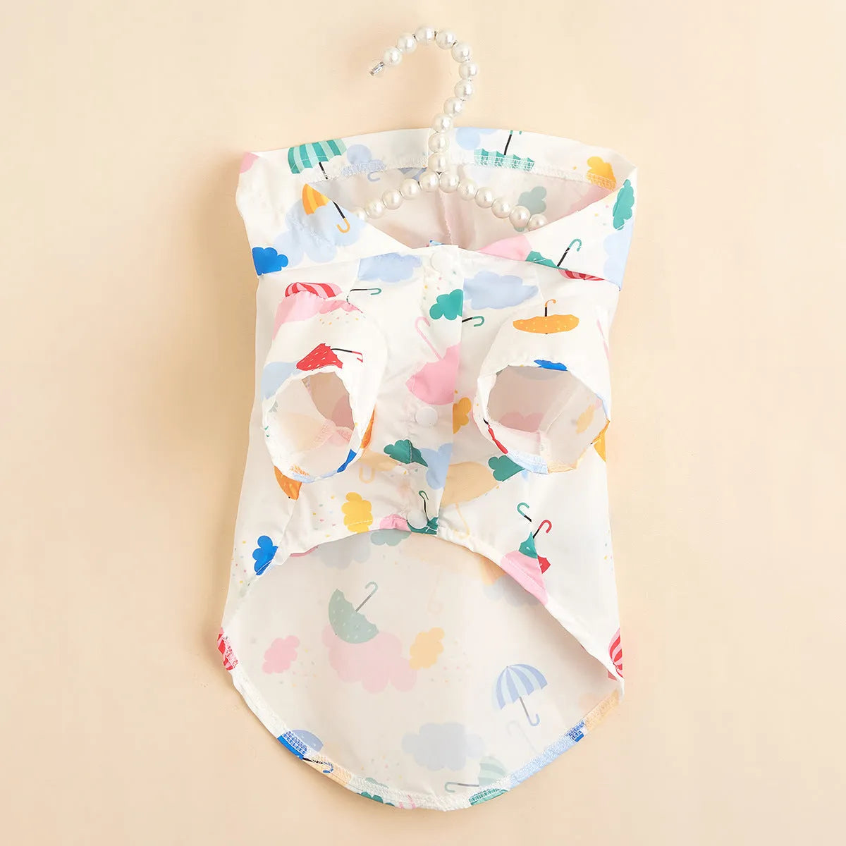 Small white dog wearing a colourful cartoon umbrella pattern polyester raincoat outdoors.