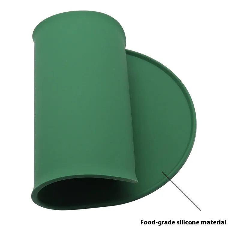 Green silicone cat feeding mat with raised edge holding a food bowl and water bowl on a kitchen floor.