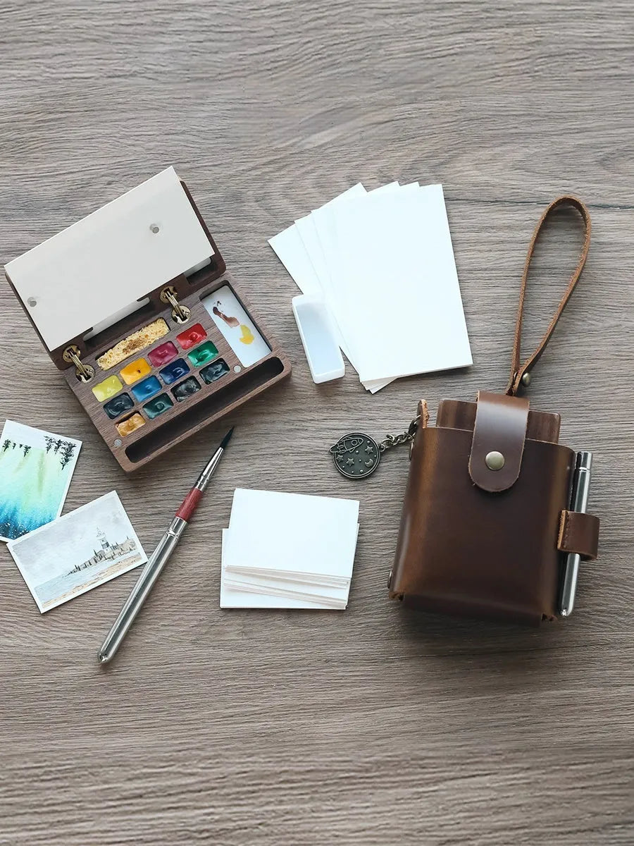 Mini walnut-finished wooden watercolour paint box open to show pigment suit pans inside.