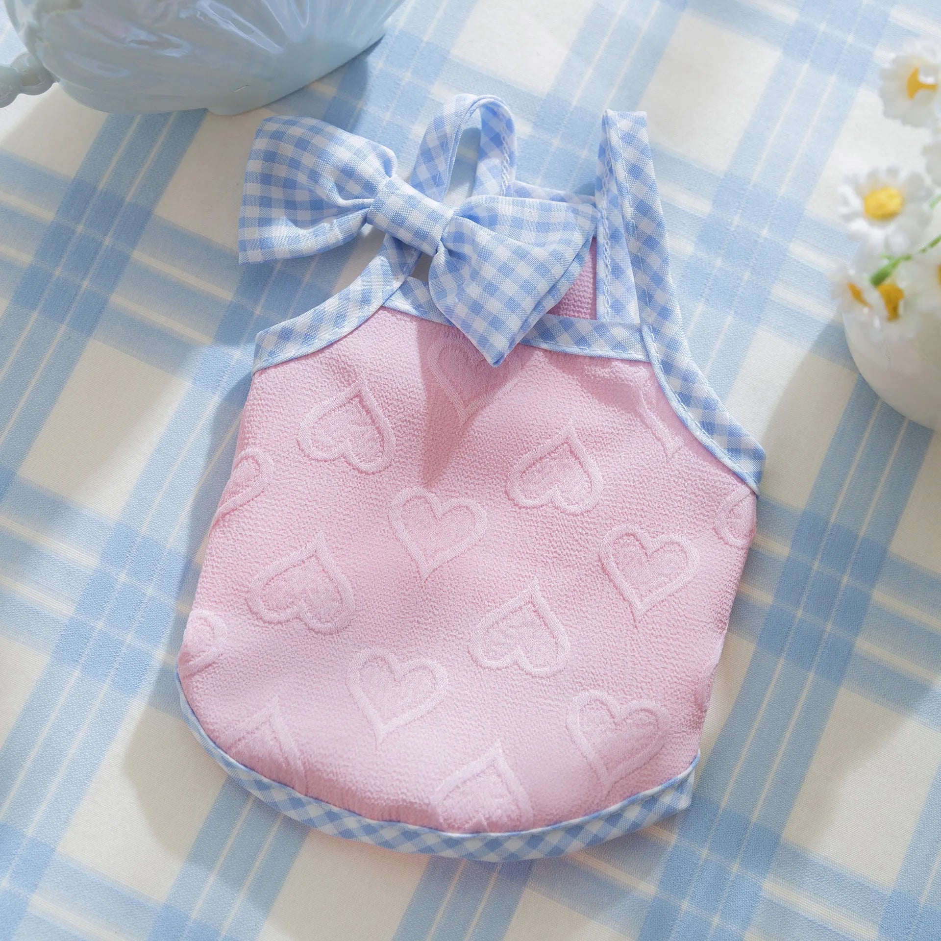 Small dog wearing a blue vest with heart texture and bow suspenders, showing adjustable elastic sides.