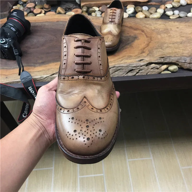 Light brown men's distressed leather lace-up shoes on a wooden surface, showing hand-carved details and round toe design.