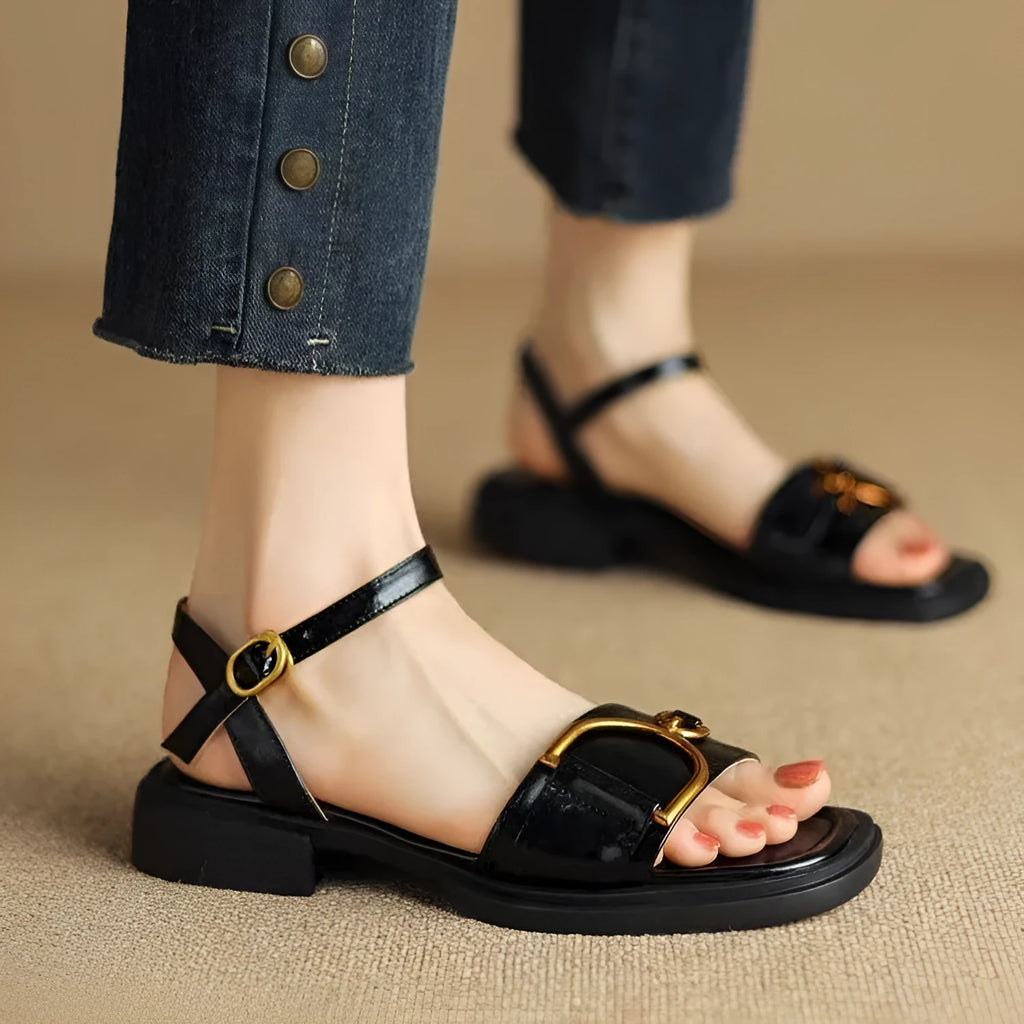 Women's black thick-soled leather sandals with a round toe and button fastening on a white background.