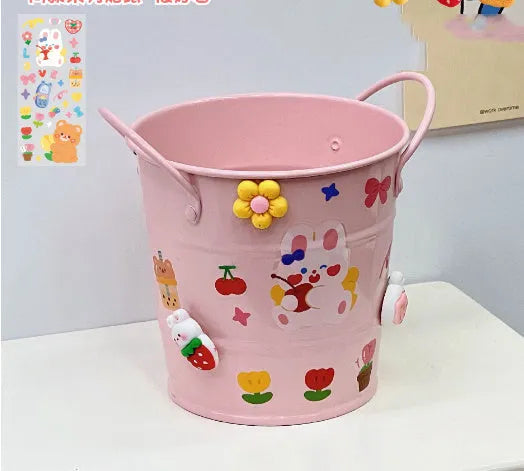 Round metal pen holder in pink with creative iron art design on a wooden desk.
