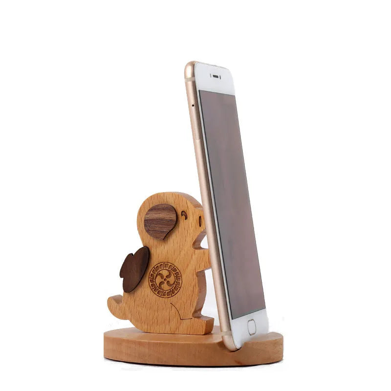 Sculpted beech wood lazy bracket phone holder with custom engraved text on a wooden desk.