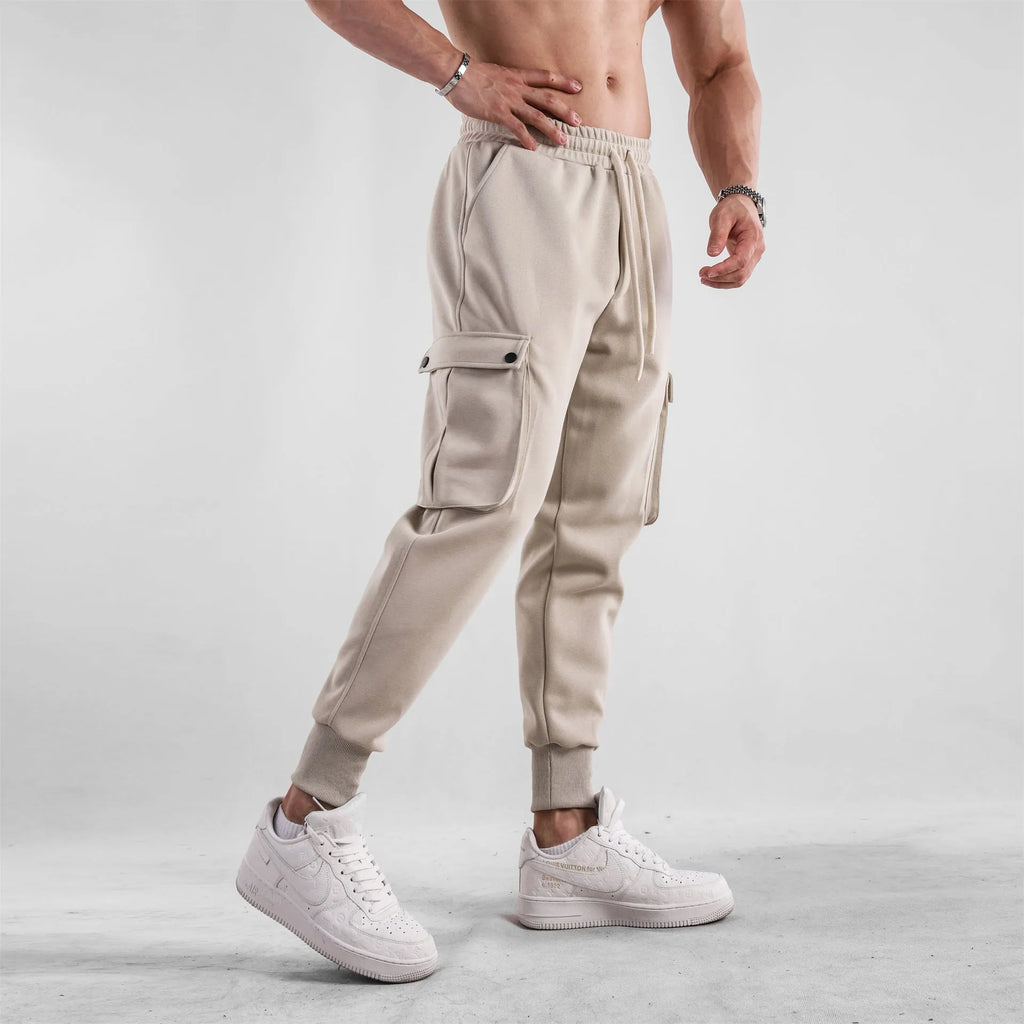 Men's loose-fit light grey cotton trousers with tapered legs and tied ankle cuffs, showing multi-pocket detail.