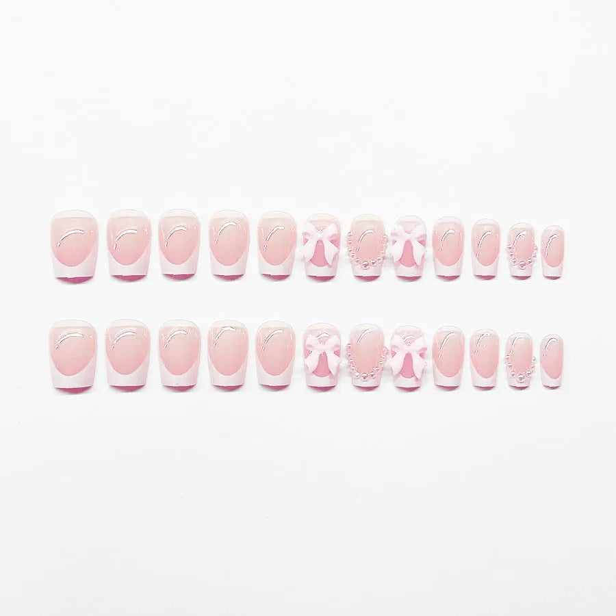 Set of white French manicure false nails with pink bow and tulip designs laid out on a table.