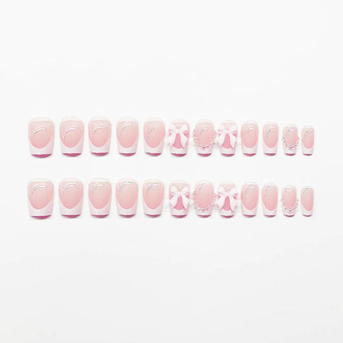 Set of white French manicure false nails with pink bow and tulip designs laid out on a table.