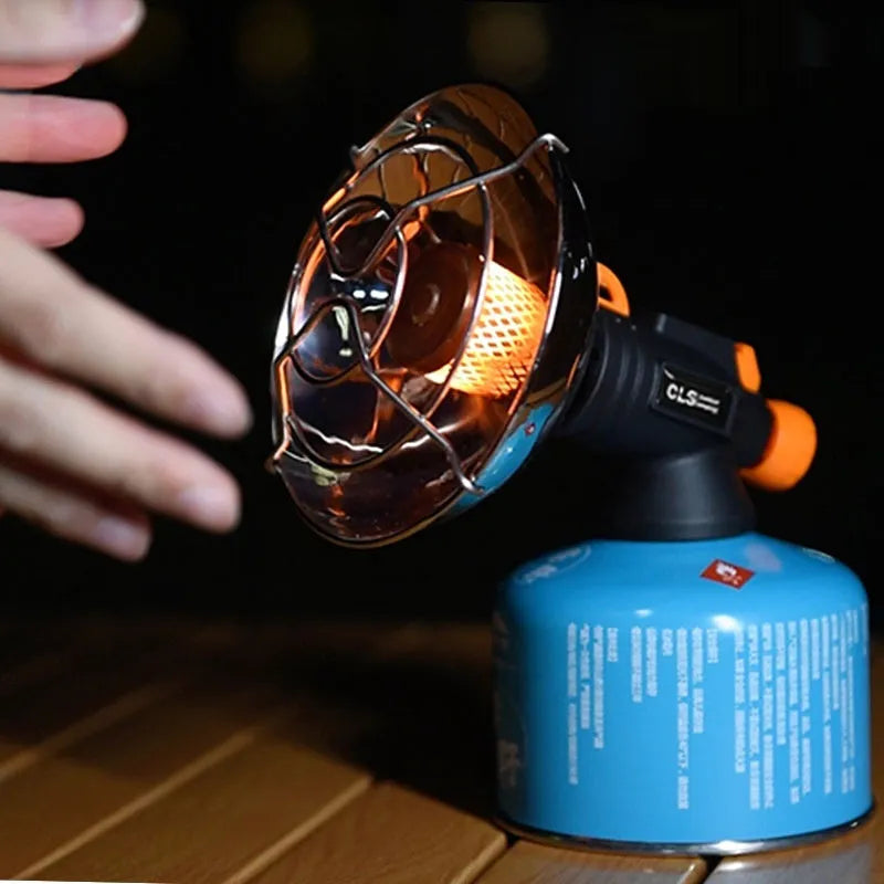 Black and orange portable camping heater stove with automatic ignition on a rocky outdoor surface.