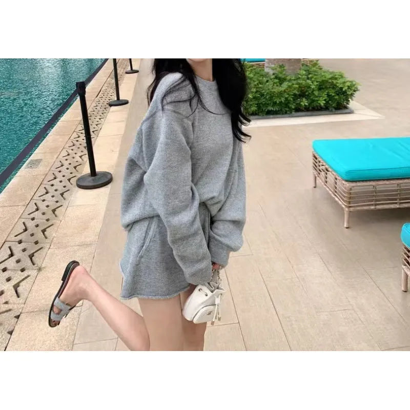 Woman wearing a loose beige knitted long-sleeve sweater and wide-leg shorts set, casual two-piece outfit.
