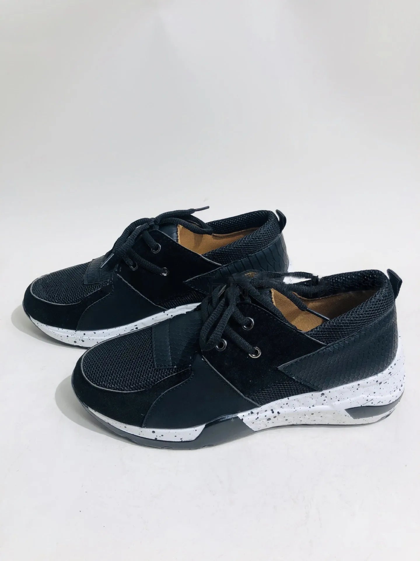 Women's black suede wedge sneakers with a round toe and low-cut design on a wooden floor.