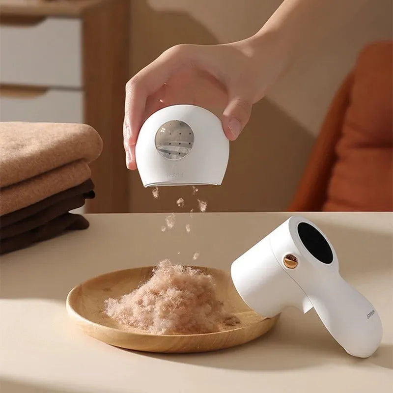 White electric lint remover with LED display showing battery level, placed beside clothing with fabric pilling