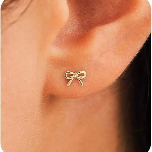 Women's gold bow stud earrings and silver cross stud earrings on a flat surface.