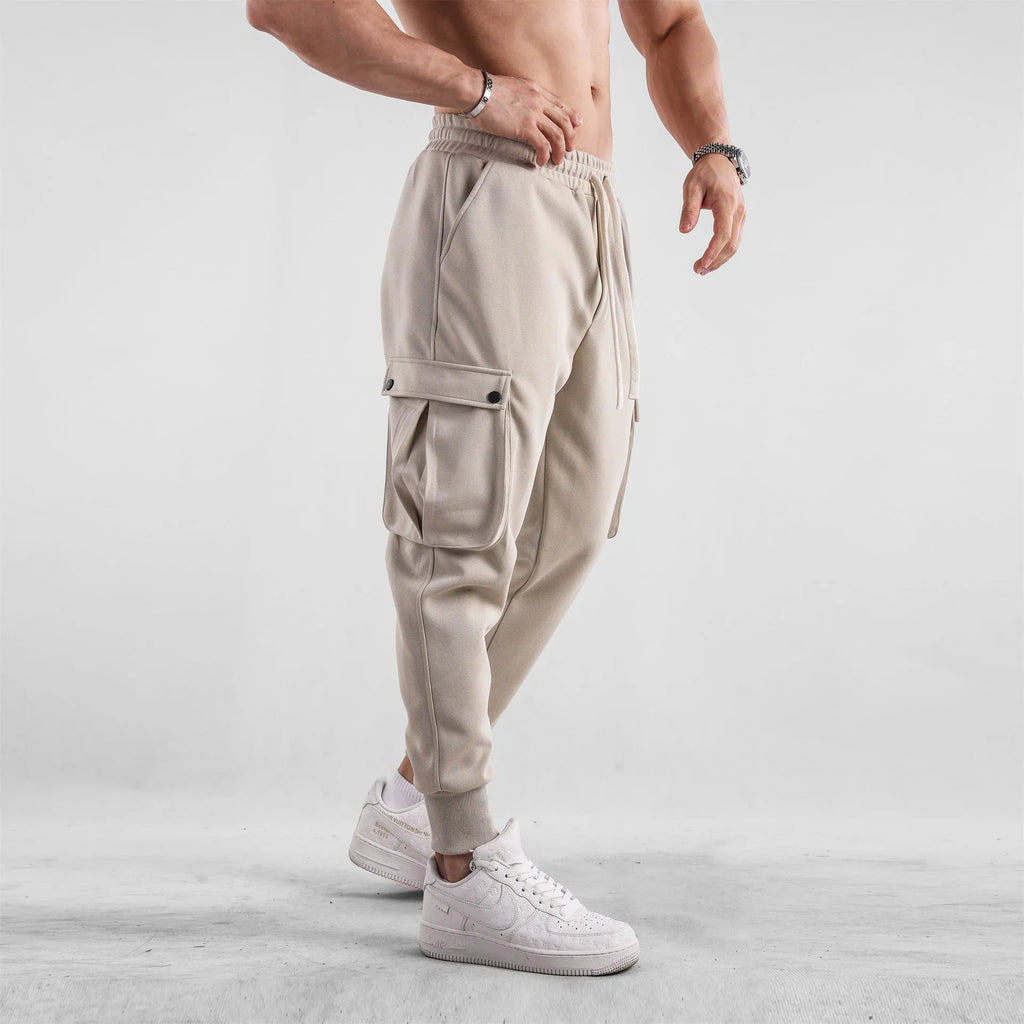Men's loose-fit light grey cotton trousers with tapered legs and tied ankle cuffs, showing multi-pocket detail.